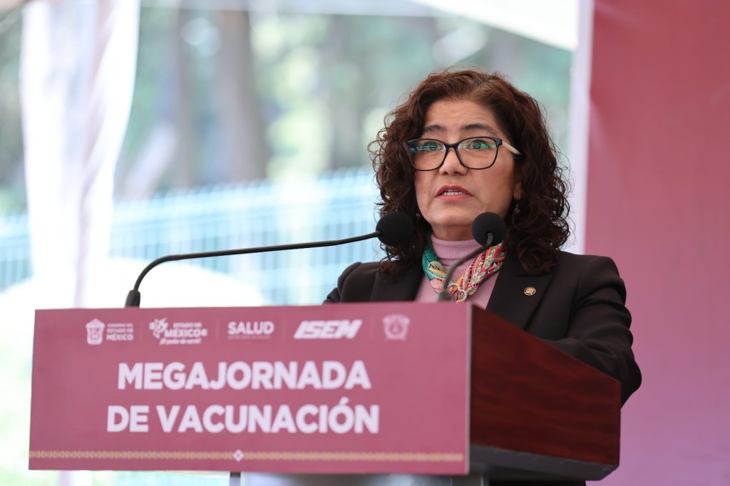 La rectora de la UAEMéx, Martha Patricia Zarza Delgado, habla en la Megajornada de Vacunación, con un fondo de color rosa que muestra el nombre del evento.