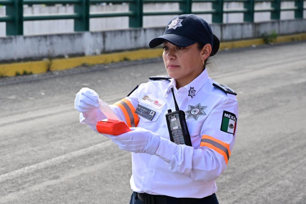 Una agente de tránsito de la Secretaría de Seguridad del Estado de México sostiene un dispositivo electrónico mientras se encuentra en una carretera.