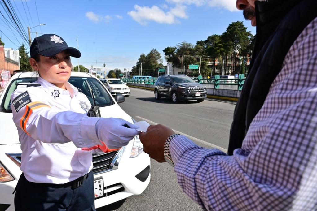 Una oficial de tránsito de la Secretaría de Seguridad del Estado de México entrega una boleta de infracción a un conductor en una vía pública.