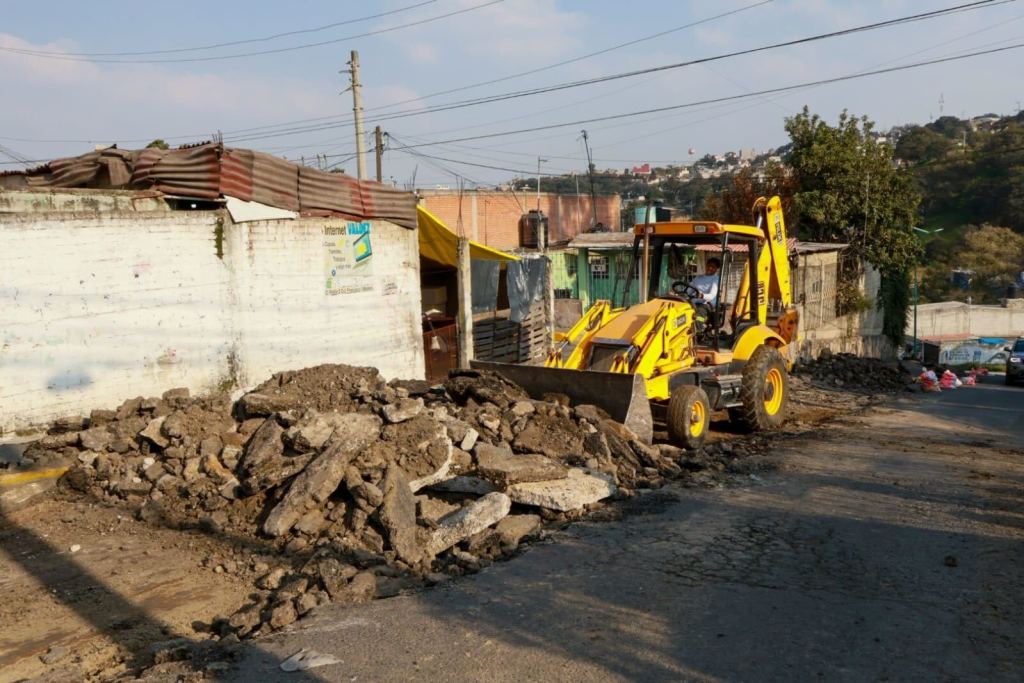 Máquina excavadora trabajando en una calle en proceso de pavimentación, con escombros y materiales de construcción a su alrededor.