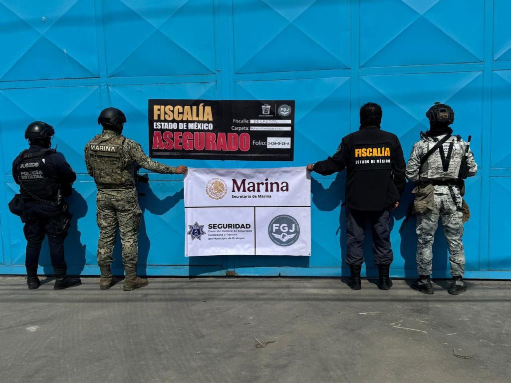 Agentes de seguridad y representantes de la Fiscalía del Estado de México frente a una puerta azul con un cartel que indica aseguramiento, durante una operación coordinada.