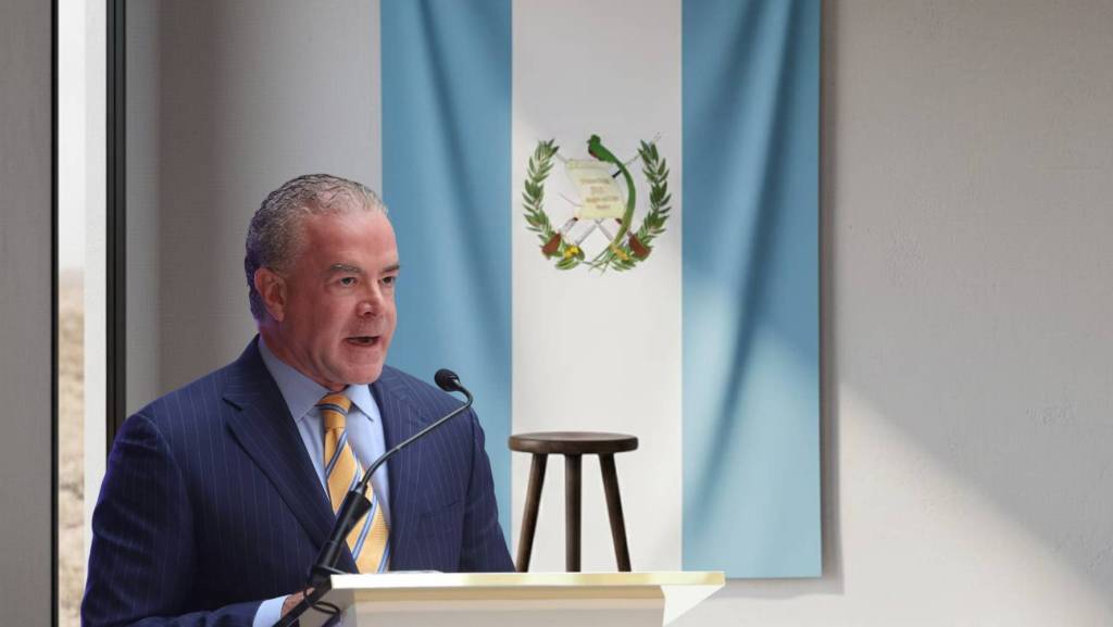 Un hombre en traje oscuro habla desde un estrado frente a una bandera de Guatemala en un evento oficial.