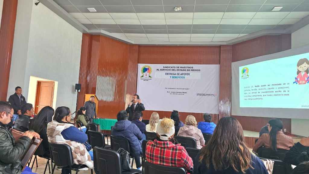 Reunión de representantes del Sindicato de Maestros al Servicio del Estado de México, con asistentes frente a un ponente en un salón, presentando una diapositiva sobre apoyos y beneficios.
