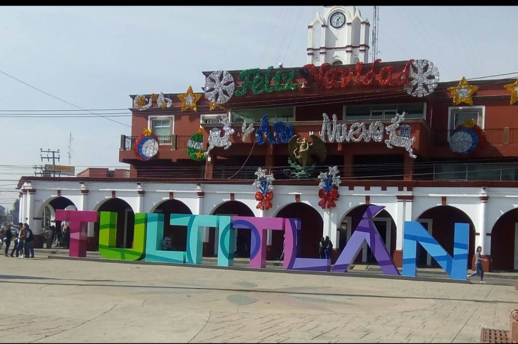 Cartel tridimensional colorido que dice 'TULTITLÁN', ubicado frente a un edificio decorado con adornos festivos en Tultitlán, Estado de México.