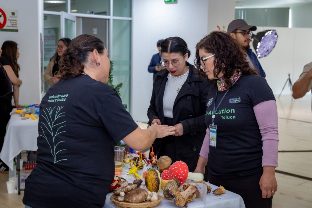 Mujeres participando en una actividad sensorial en el evento 'Evolución para todas y todos', con mesas llenas de materiales educativos y elementos naturales.