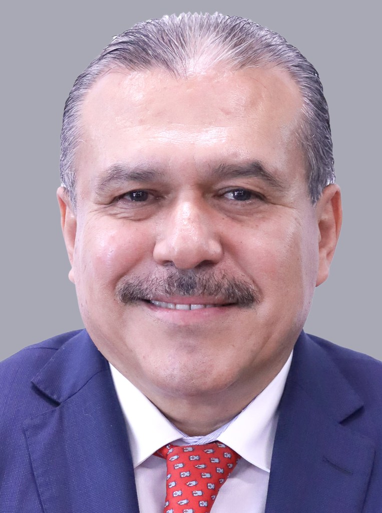 Retrato de un diputado federal mexicano, sonriendo, con cabello corto y vestido con traje y corbata roja.