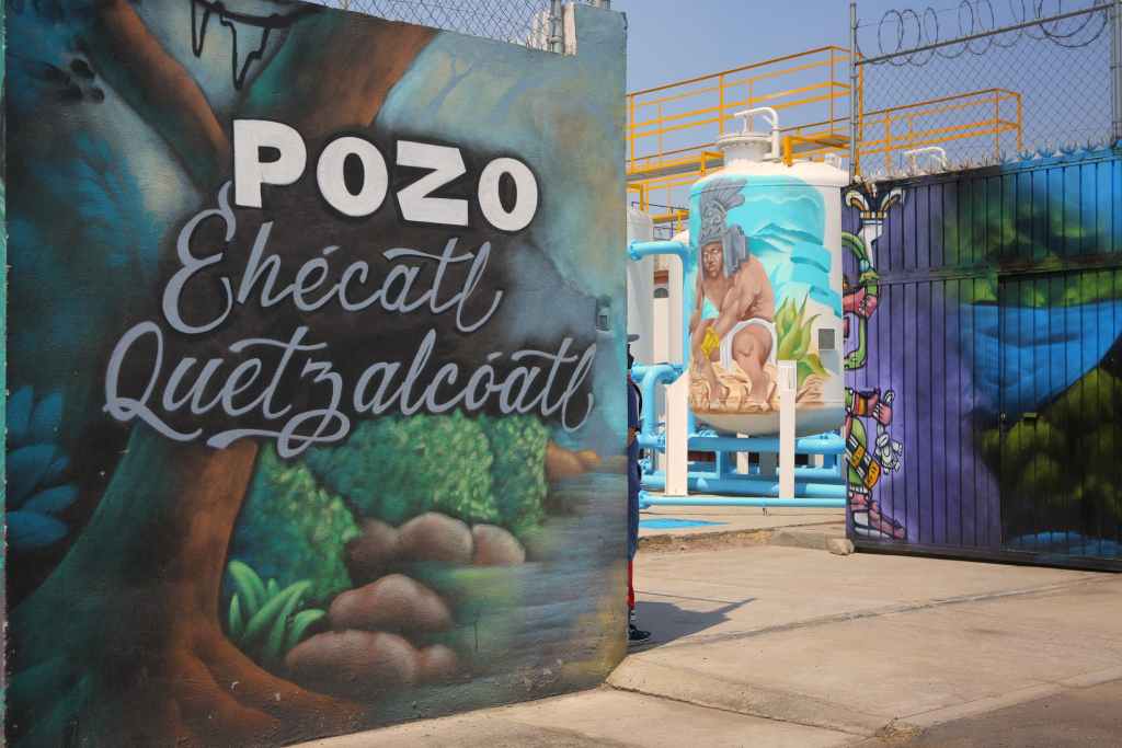 Mural en un pozo de agua en Ecatepec, con el nombre 'Ehécatl Quetzalcóatl' en letras decorativas, rodeado de ilustraciones coloridas de figuras y naturaleza.
