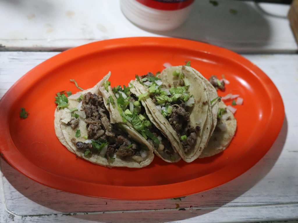 Plato con varios tacos de carne, servidos en un plato naranja, decorados con cebolla y cilantro.