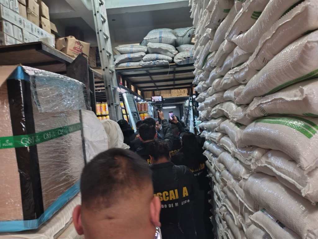 Interior de un almacén durante la Operación SENDA, mostrando a varios agentes de la fiscalía en un pasillo estrecho entre sacos de mercancía apilados.