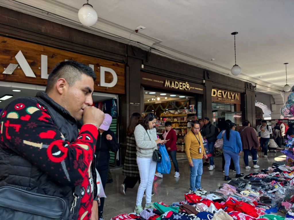 Un grupo de compradores en Los Portales de Toluca, mirando productos navideños, como ropa y zapatos, en un ambiente de compras animado.