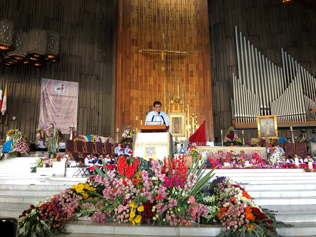 Un hombre habla en un altar decorado con flores en la Basílica de Guadalupe durante la celebración del 12 de diciembre.
