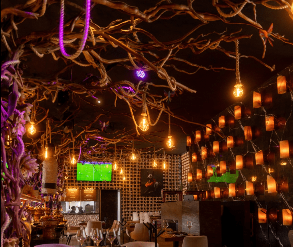 Interior del restaurante con decoración rústica, luces colgantes y pantallas que muestran un partido de fútbol.