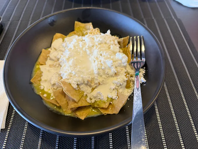 Un plato de chilaquiles verdes servidos en un tazón negro, cubiertos con crema y queso fresco.