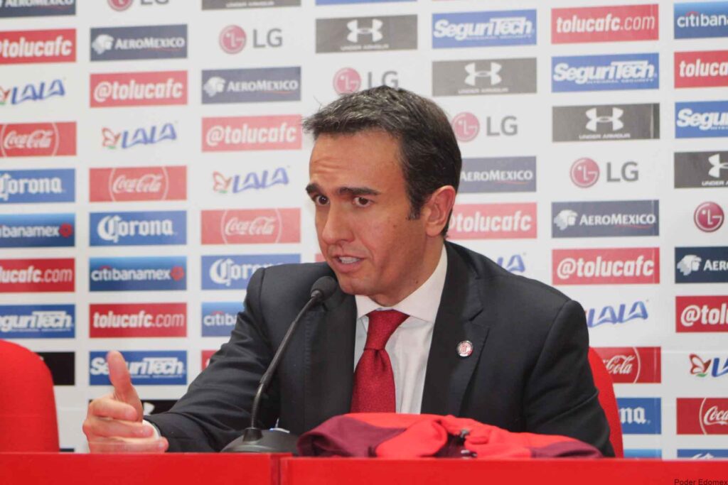 Un directivo de Toluca habla en una conferencia de prensa, con un fondo de logotipos relacionados con el equipo y patrocinadores.