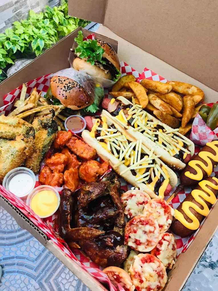 Una cajita con una variedad de platillos que incluye alitas, hamburguesas, papas fritas, aros de cebolla y mini pizzas, presentados de manera colorida y organizada.