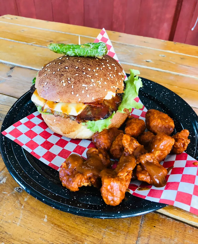 Plato que contiene una hamburguesa con lechuga, frituras y alitas de pollo con salsa, servido en un plato negro con un fondo de mesa de madera.