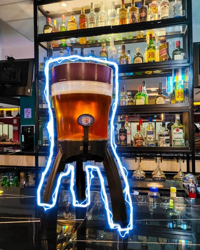 Una gran jarra de cerveza en un bar, con una estantería de botellas de licor de fondo.