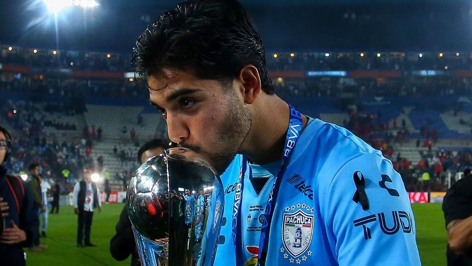Jugador sosteniendo y besando un trofeo, con un fondo de estadio y afición celebrando.