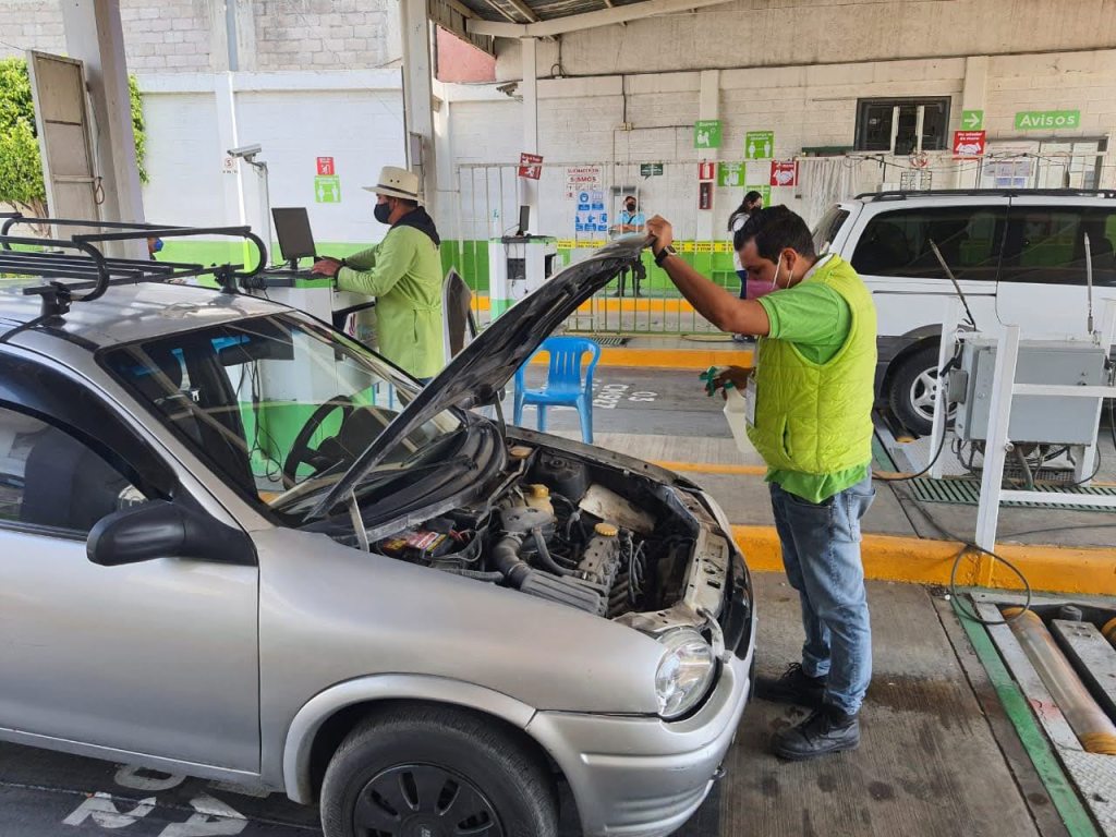 Técnico revisando el motor de un automóvil en un centro de verificación vehicular.