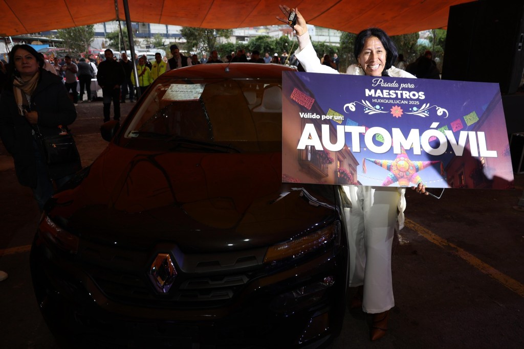 Una mujer sonriente sostiene un cartel que dice 'Válido por un AUTOMÓVIL' frente a un auto Renault, mientras una multitud observa alrededor en un evento de rifa en Huixquilucan.