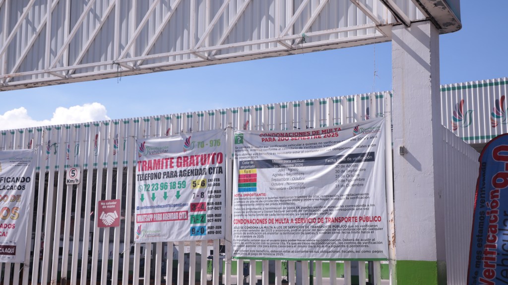 Entrada de un verificentro en Toluca con anuncios sobre trámites gratuitos, condonaciones de multas y horarios de verificación.