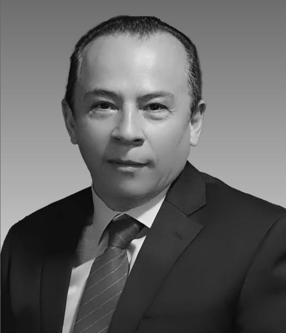 Retrato en blanco y negro de un hombre con traje y corbata, sonriendo ligeramente, sobre un fondo gris.