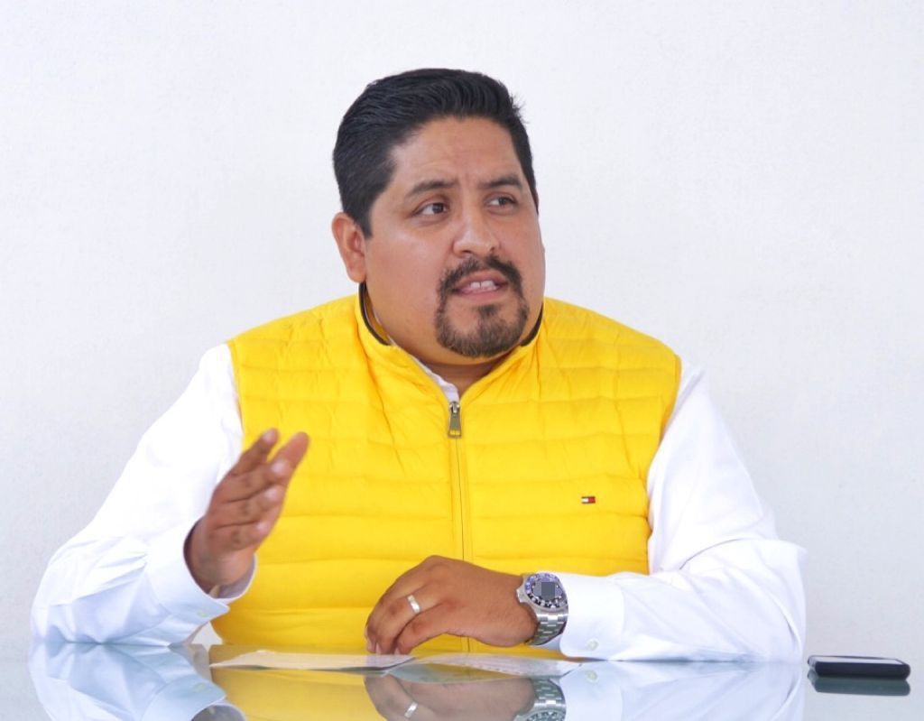 Jacobo Reyes León, excandidato a la alcaldía de San Martín de las Pirámides, en una reunión, vistiendo un chaleco amarillo y una camisa blanca, gesticulando mientras habla.