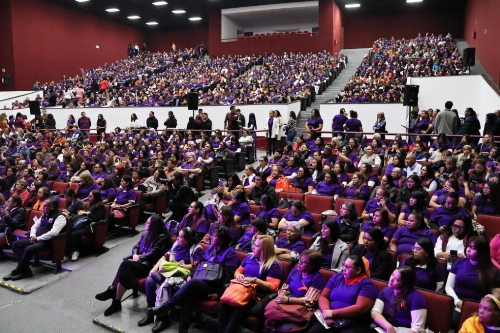 Gran audiencia de mujeres vestidas de morado en un evento, mostrando participación comunitaria y enfoque en la prevención del delito.