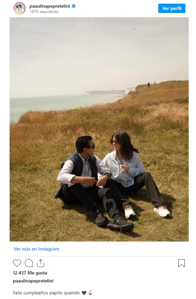 Una pareja sentada en un campo, disfrutando de la vista del océano. Se ven felices, mientras conversan y se miran con afecto.