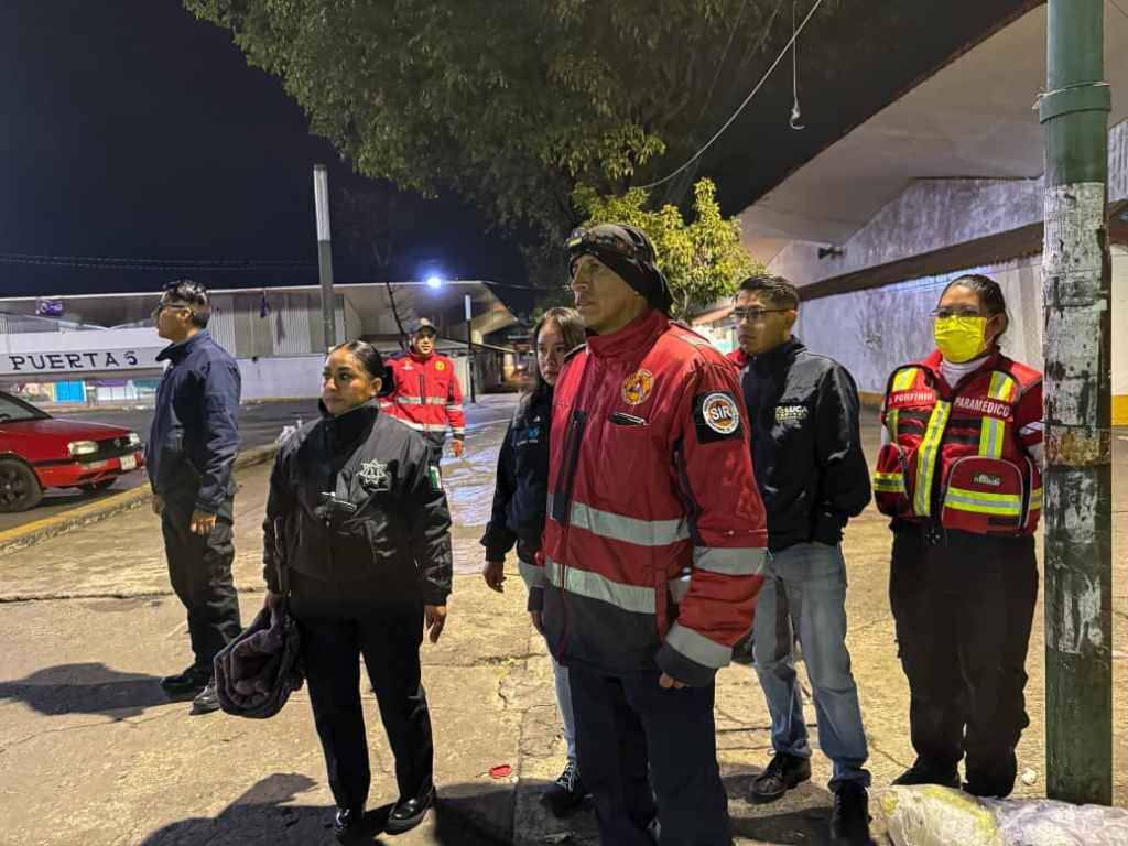 Grupo de personas, incluyendo a miembros de la policía y protección civil, reunidos en la calle durante la noche, preparados para realizar rondines de búsqueda de personas en situación vulnerable en Toluca.