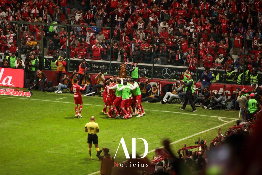 Jugadores de Toluca celebrando en el campo rodeados por una multitud de aficionados en las gradas, con un ambiente festivo y lleno de emoción en el estadio.