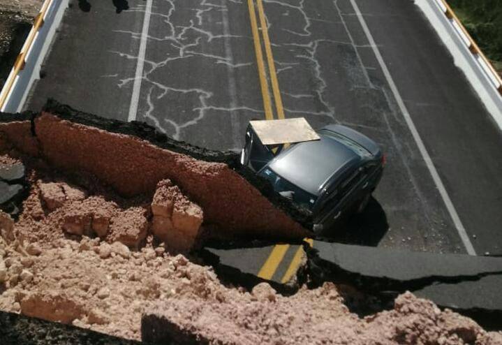 Un automóvil detenido en una carretera colapsada, con un gran socavón visible que divide la vía en dos secciones.