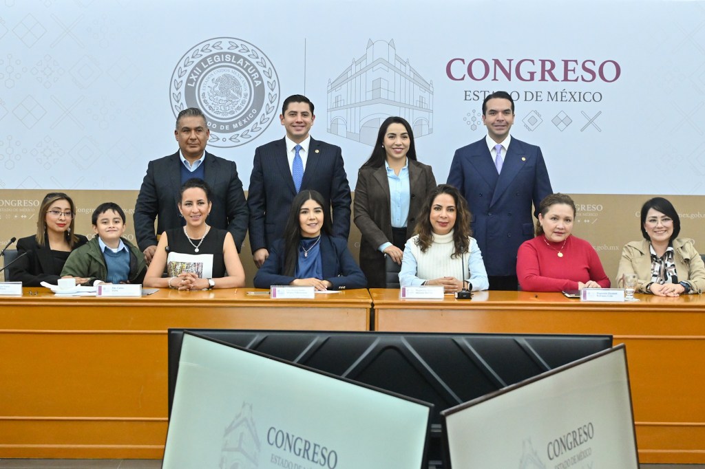 Grupo de personas posando en el Congreso del Estado de México, con una mesa y computadoras en primer plano.