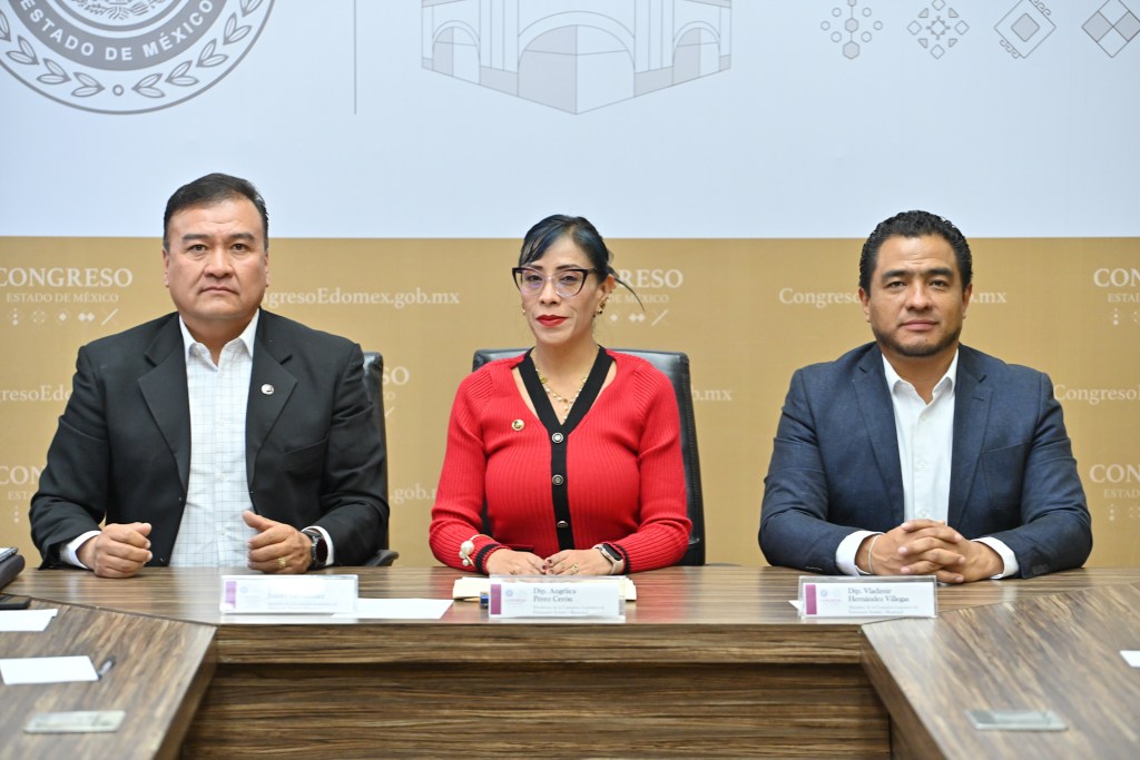 Tres legisladores sentados en una mesa durante una reunión en el Congreso del Estado de México, con un fondo institucional.