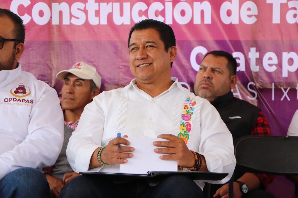 El alcalde de Ixtapaluca, Felipe Arvizu de la Luz, sonriendo durante un evento público, con un fondo que dice 'Construcción de Taminé' en un stand al aire libre.