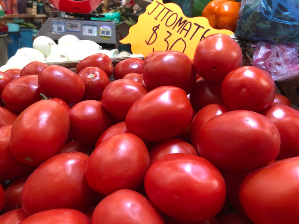 Toma de jitomates frescos en un mercado, con un letrero que indica el precio de $30.