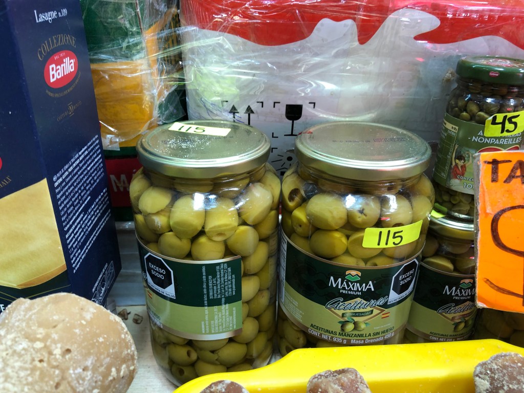 Tarros de aceitunas manzanilla en un mercado, etiquetados con precios.