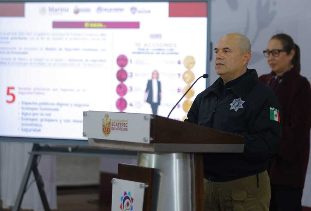 Comisario de Seguridad Ciudadana, Edgar Machado Peña, dando una conferencia de prensa sobre la reducción de delitos en Ecatepec, con gráficos y datos en pantallas de fondo.
