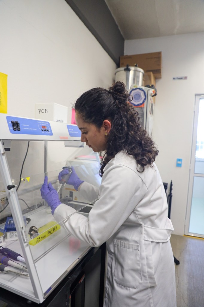 Una estudiante de biotecnología trabajando en un laboratorio, utilizando herramientas de laboratorio y vestimenta adecuada.