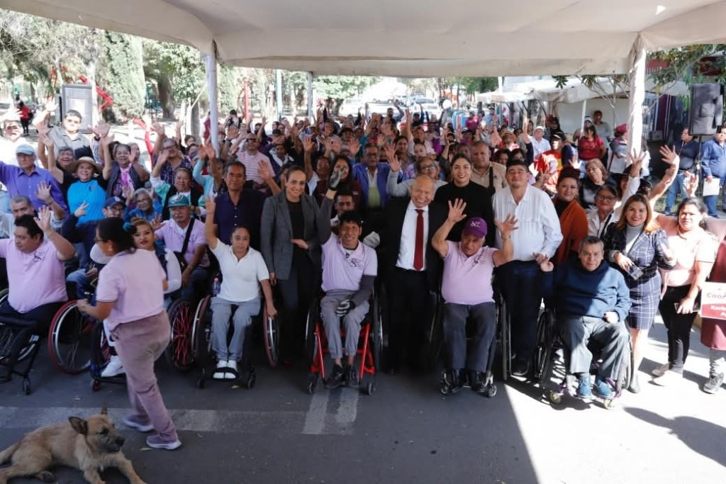 Gran reunión de personas en el evento de las Cocinas del Bienestar en Tlalnepantla, con integrantes de la comunidad levantando las manos y sonriendo, junto a autoridades locales.