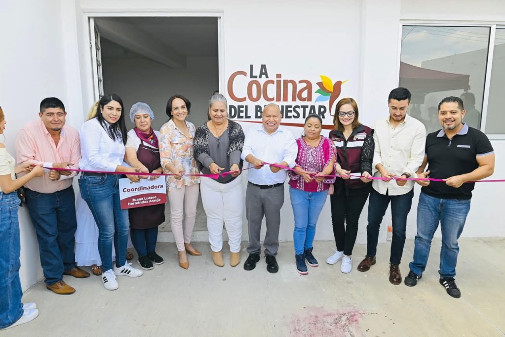 Inauguración de una cocina comunitaria con varias personas sosteniendo una cinta para cortar en un evento de celebración.