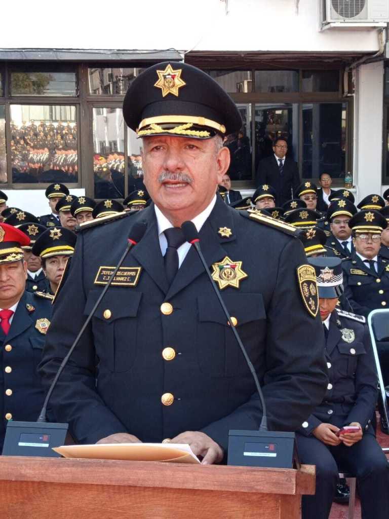 Un funcionario de CUSAEM, vestido con uniforme de policía, habla ante un micrófono mientras es observado por otros oficiales sentados detrás de él en un evento oficial.