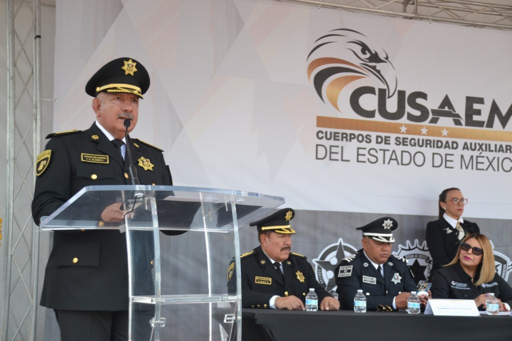 Un funcionario de CUSAEM habla en un evento, acompañado de otros oficiales, frente a un fondo con el logo de la corporación.