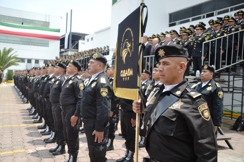 Ceremonia de la Policía Auxiliar del Estado de México, con elementos alineados y un oficial sosteniendo la bandera de CUSAEM en primer plano.