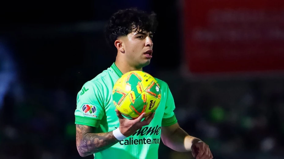 Denzell García sosteniendo un balón de fútbol, con uniforme verde, durante un partido.