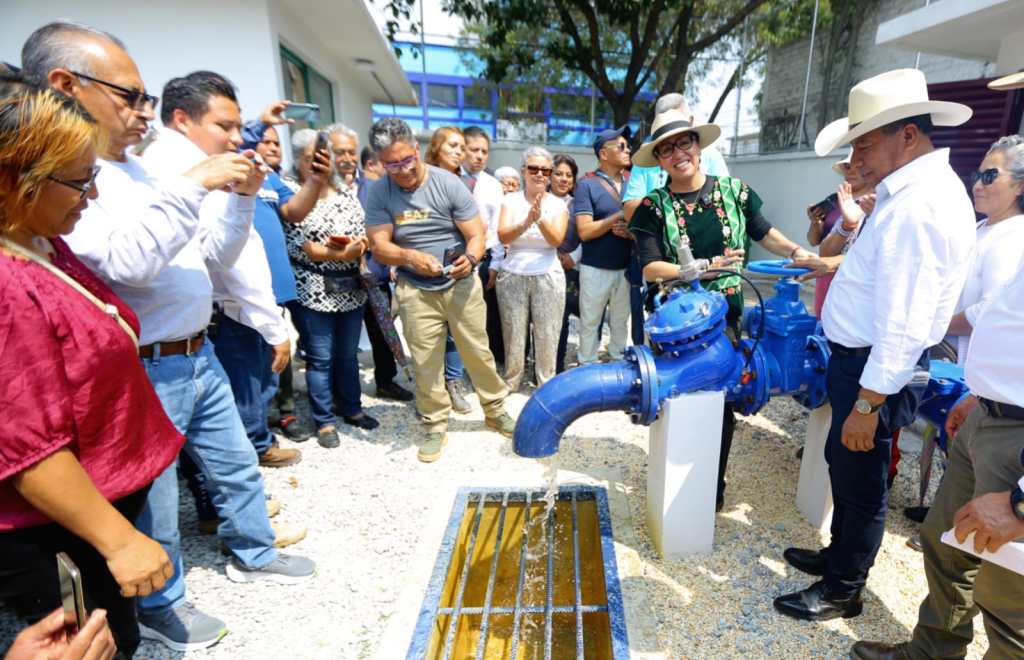 La alcaldesa Azucena Cisneros Coss inaugurando un nuevo sistema de suministro de agua potable en Ecatepec, con un grupo de personas observando y tomando fotos.