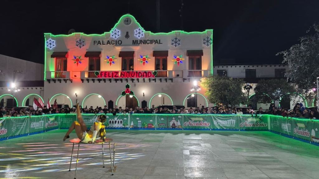 Vista del Palacio Municipal decorado con luces navideñas durante la inauguración de una ecopista de patinaje, con una persona realizando una actuación sobre hielo y un público animado en la explanada.