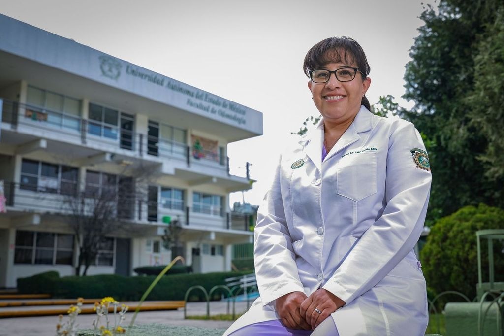 Edith Lara Carrillo, profesora e investigadora de la Facultad de Odontología de la UAEMéx, posa frente al edificio de la universidad en bata blanca.