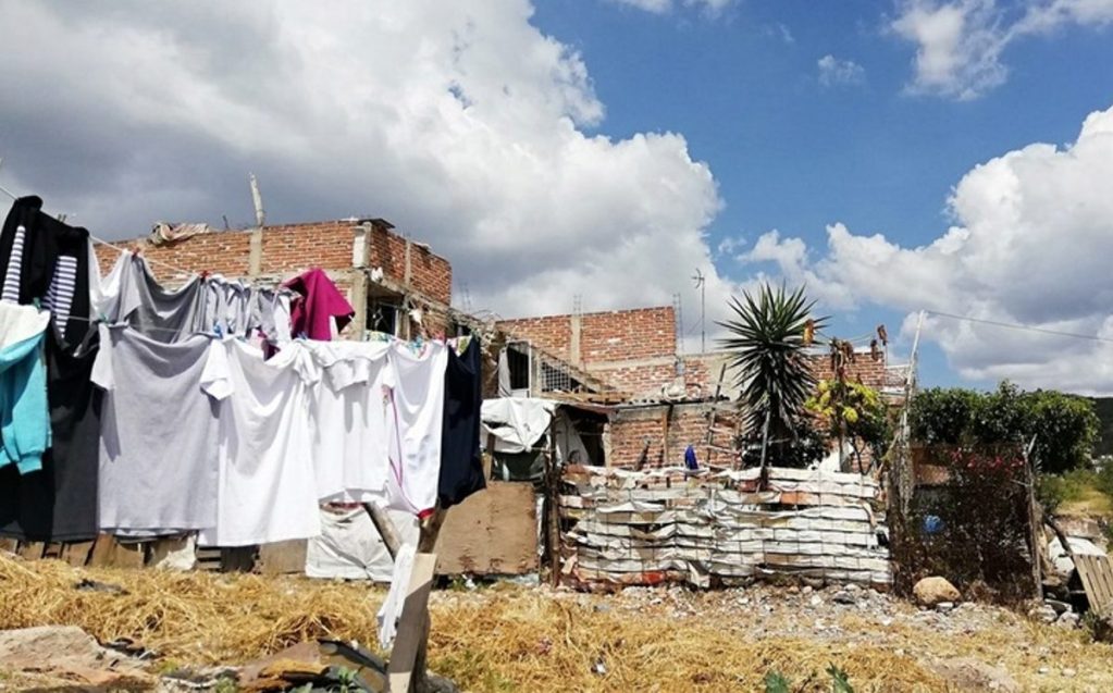 Vista de una zona vulnerable con ropa tendida al sol, casas de ladrillo y un cielo nublado en el fondo.