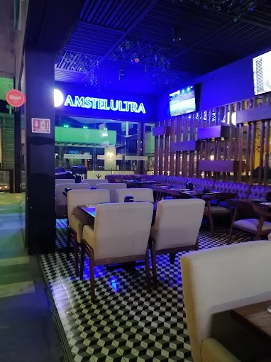 Interior de un restaurante con mesas y sillas, iluminado y decorado, con logotipo de Amstel Ultra en la pared.